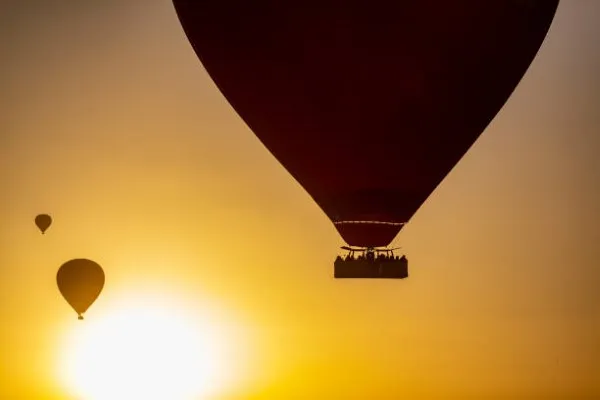 Tres globos aerostáticos volando sobre un atardecer en los celos por pasajeros que disfrutan de un paseo en globo aerostático..
