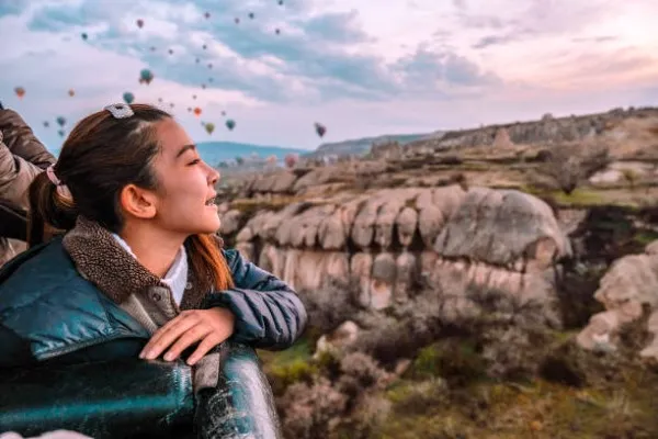 Niña con una chamarra abrigadora, recargada sobre la canasta de un globo aerostático. Feliz y sonriente, disfrutando de un viaje inolvidable en los cielos de Teotihuacan.