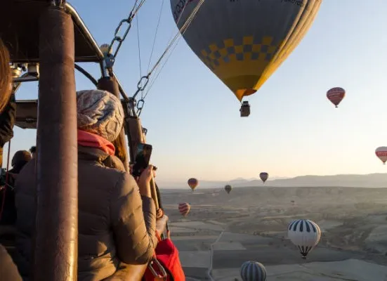 Mujer dentro de la canasta de un globo aerostático después de solicitar un vuelo compartido. Capturando el amanecer en un video.