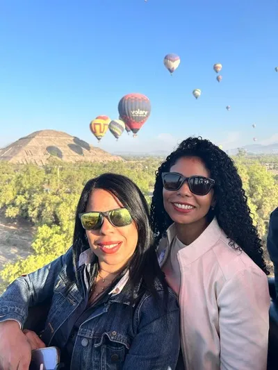 Amigas disfrutando de las vistas que tiene Teotihuacan para ofrecer en un amanecer en globo aerostático con más globos flotando alrededor.