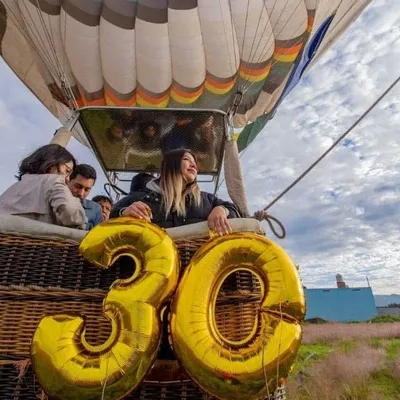 Mujer festejando su cumpleaños número 30 con globos dorados sobre un globo aerostático, una de las tantas actividades en teotihuacan que puedes realizar.