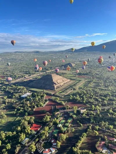 People inside hot air balloons Teotihuacan enjoying a clear sunrise while flying over the Sun and Moon pyramids.