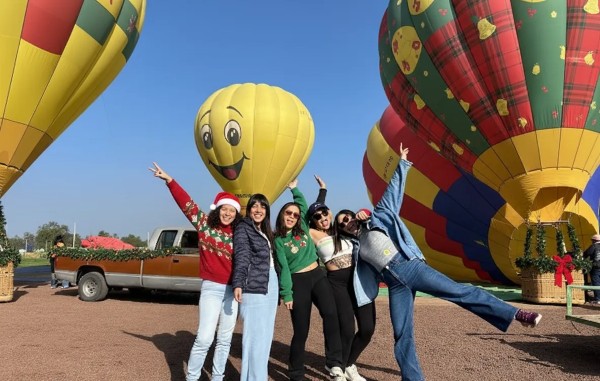 Tres amigas con suéteres navideños posan felices antes de iniciar sus vuelos en globo para navidad al atardecer.