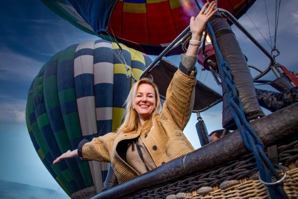 A smiling woman enjoys her first hot air balloons ride, celebrating a personal experience with spectacular views.