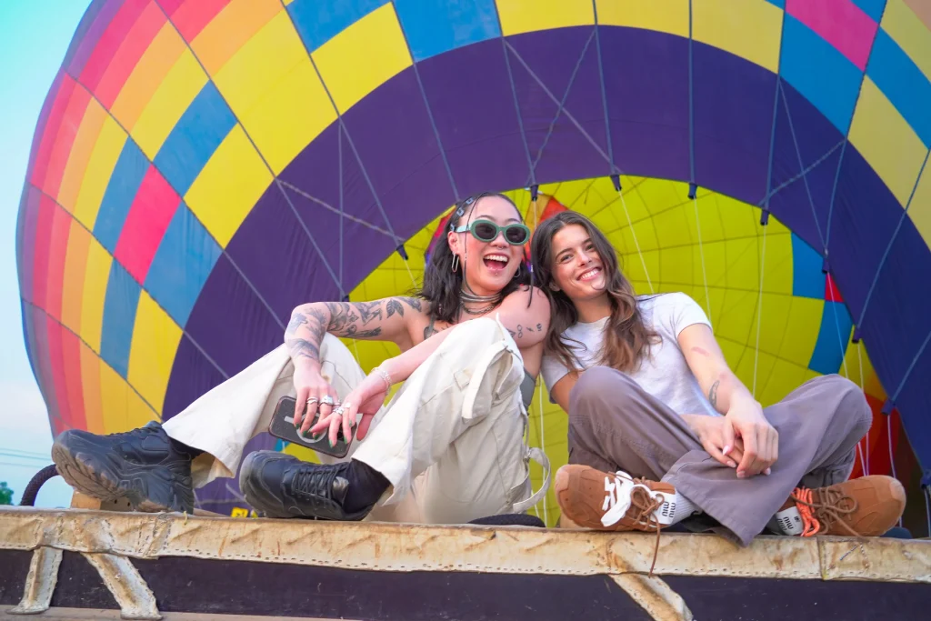 Dos amigas sentadas en una canasta disfrutan la experiencia usando vestimenta para un vuelo en globo adecuada y cómoda.