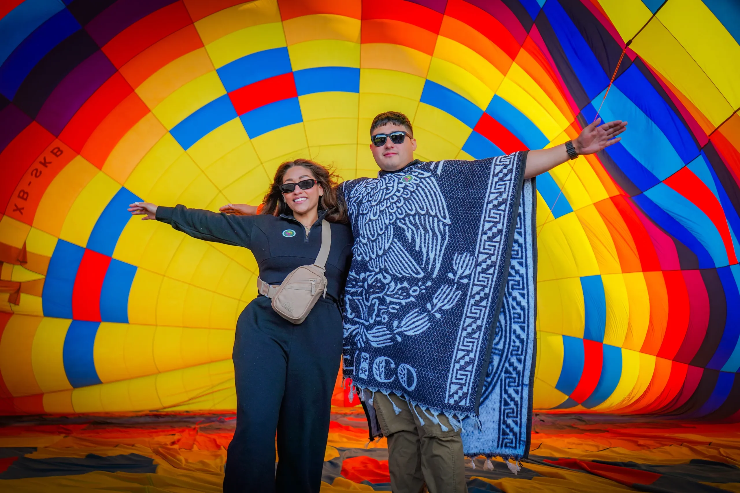 Pareja sonriente prepara experiencia de vuelo en globo al amanecer Teotihuacán observando globos coloridos antes del despegue matutino.