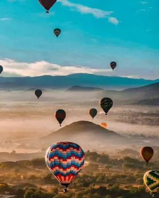 Vista panorámica del festival de globos aerostáticos flotando sobre las antiguas pirámides de Teotihuacán.
