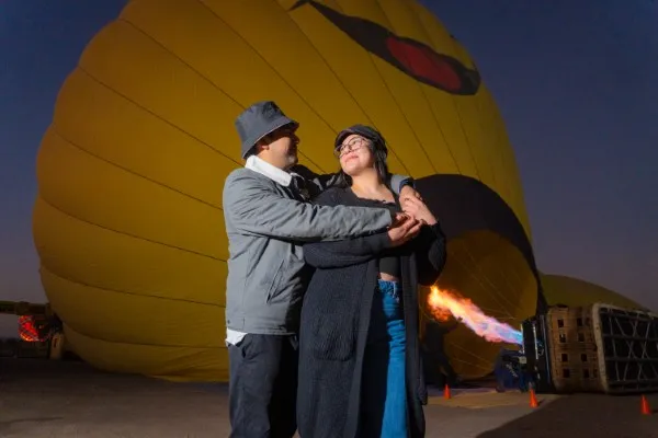 Couple embracing, capturing a special memory on a hot air balloon ride during Easter with colorful balloons in the background.