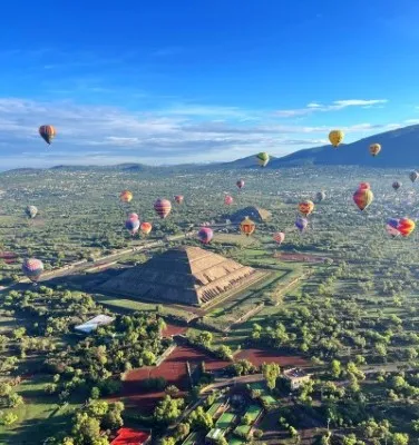 Aerial view of hot air balloon ride in Teotihuacán over the pyramids at sunrise, with numerous colorful balloons rising into the sky.